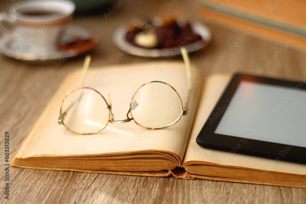 Books, reading glasses, e-reader, plate of chocolate pralines, bowl of cookies, cups of tea and lit candles on the table. Selective focus. Books, reading glasses, e-reader, plate of chocolate pralines, bowl of cookies, cups of tea and lit candles on the table. Selective focus.