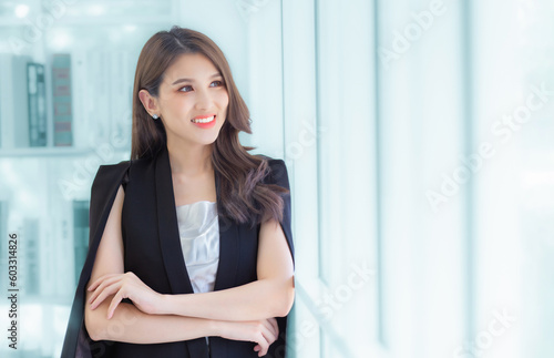 Work from home. Professional business Asian young office lady is standing crossed arms looking out the window confident and smiling at work happily. © nut_foto