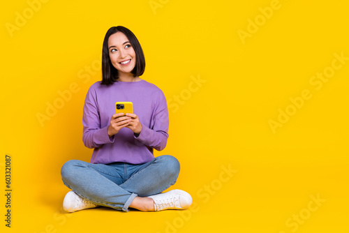 Photo of dreamy adorable lady dressed purple shirt texting modern device looking empty space isolated yellow color background