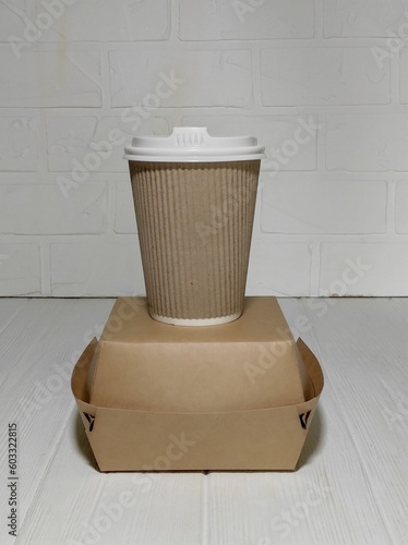Disposable paper cup with lid stands on paper food container
