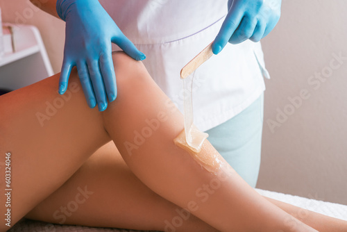 Hands of a cosmetologist close-up, in blue gloves, applying sugar paste on a woman's leg. Depilation procedure