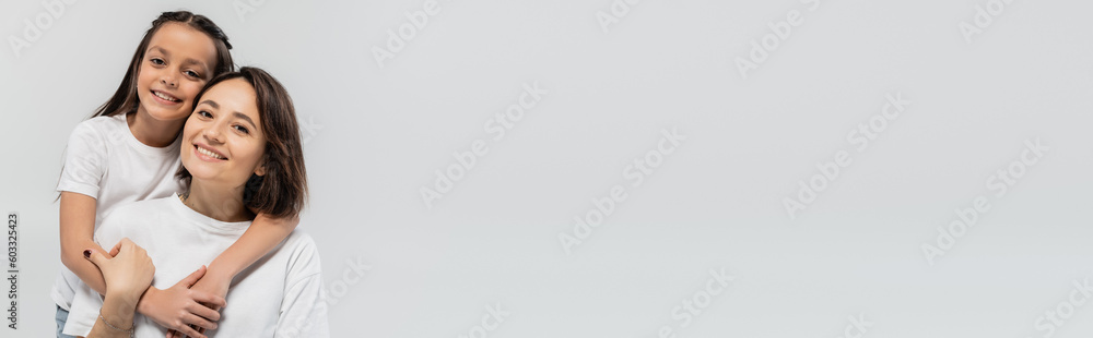 preteen girl with brunette hair hugging happy mother with short hair while posing together in white t-shirts and looking at camera on grey background, international children's day, banner preteen girl with brunette hair hugging happy mother with short hair while posing together in white t-shirts and looking at camera on grey background, international children's day, banner