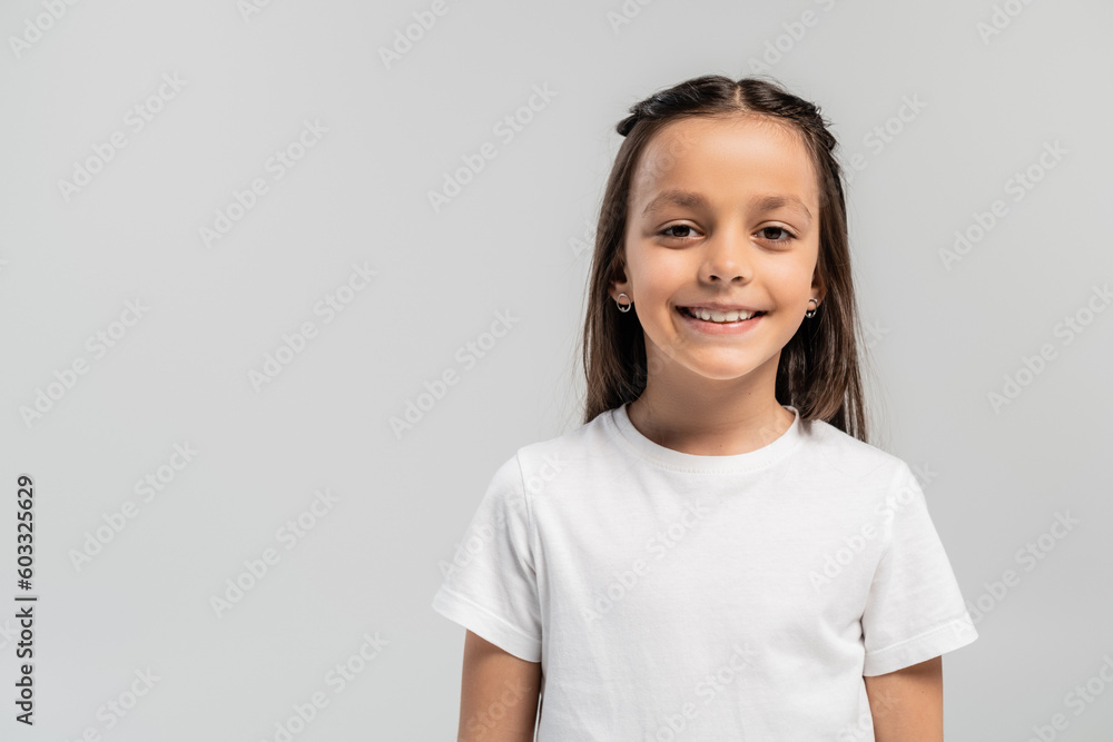 Portrait of smiling preteen and brunette girl in white t-shirt looking at camera while celebrating global child protection day isolated on grey with copy space Portrait of smiling preteen and brunette girl in white t-shirt looking at camera while celebrating global child protection day isolated on grey with copy space