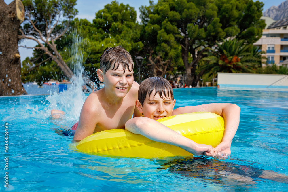 Two kids boys having fun on inflatable rubber rings in outdoor pool. Summer holiday. Summertime kids weekend. Children having fun, brothers on family vacations.