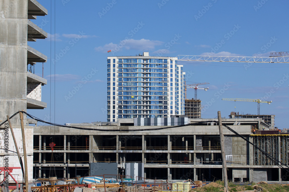 Construction site. Reinforced concrete frames of multi-storey buildings and construction cranes. The final stage of construction. Against the background of the blue sky.