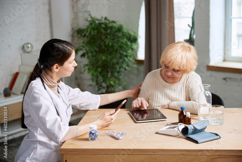 Senior woman and female doctor using gadgets to check patient's health information. In office. Modern medical attitude. Concept of medical care, medicine, illness, health care, profession