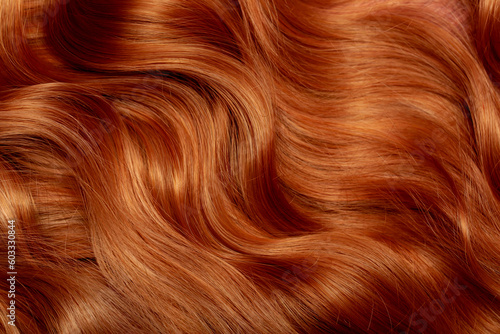 Red hair close-up as a background. Women\'s long orange hair. Beautifully styled wavy shiny curls. Hair coloring bright shades. Hairdressing procedures, extension.