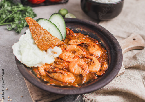 Udang sambal gami or spicy prawn is Traditional food from Indonesia. served on plate with a bowl of rice and vegetables. Isolated gray background photo