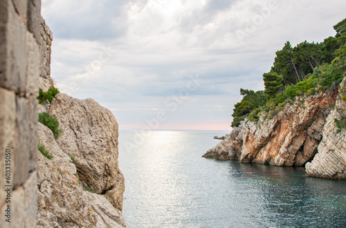 Landscape scenery of coastal rock under forest, calm sea water and stormy clouds in the horizon. Summer beauty of adriatic seaside nature.