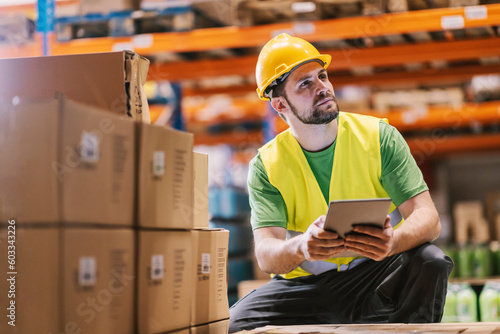 A warehouseman crouching and adding orders for export on list on tablet.