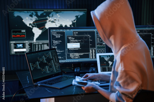 With currency in hands. Young professional female hacker is indoors by computer with lot of information on displays