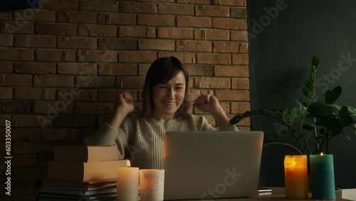 Happy caucasian woman using laptop at home during electricity outage or blackout with lit candles. Inspired woman raises her hands up after goal achievement. Success concept photo
