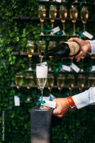 A waiter in a white shirt pours champagne into a glass on the background of a wall with glasses. Holiday in a restaurant