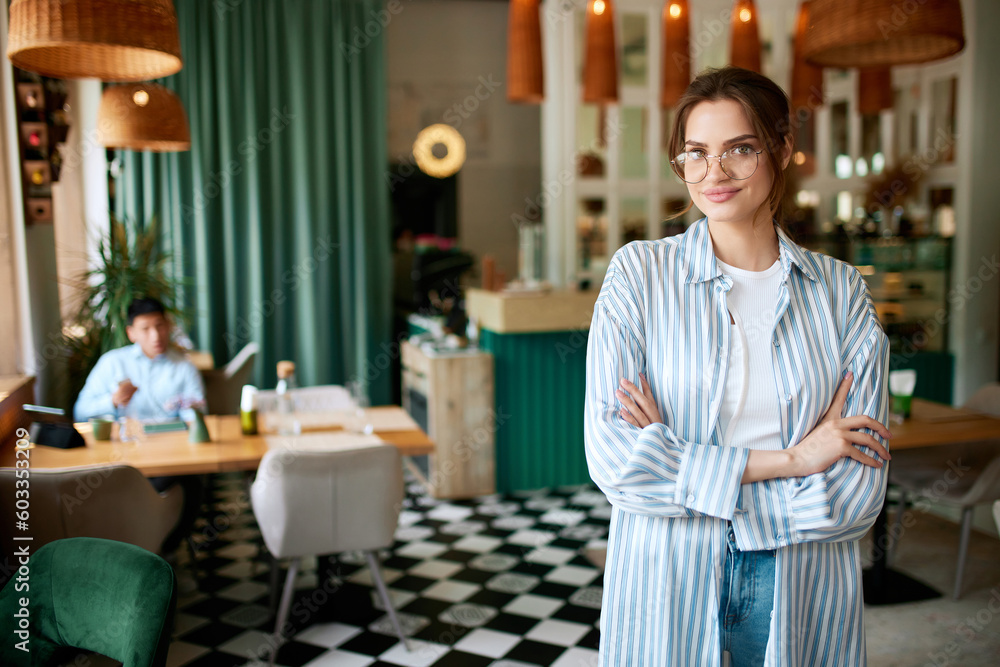 Fototapeta premium One confident girl, businesswoman wearing casual clothes standing with folded hands and smiling over city cafe background