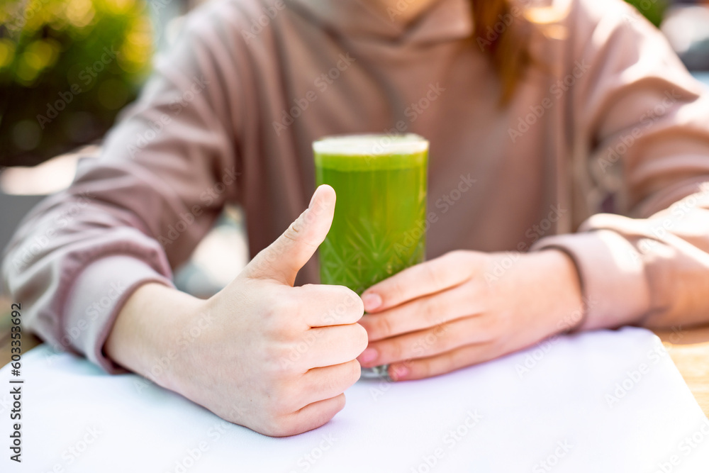 closeup thumb up hand holding green fresh smoothie. unrecognizable woman in sportswear drinks nutritional shake after workout closeup thumb up hand holding green fresh smoothie. unrecognizable woman in sportswear drinks nutritional shake after workout