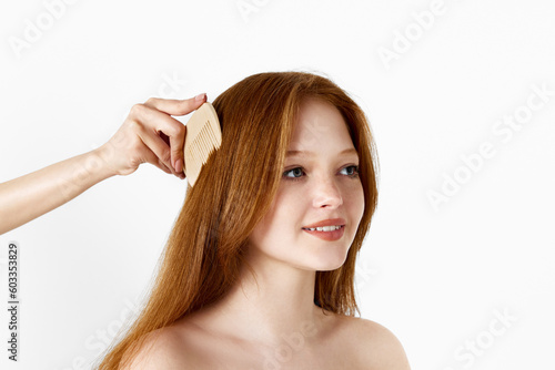 Female hand brushing hair of beautiful, tender redhead girl against white studio background. Haircare cosmetics. Concept of natural beauty, hair care, treatment, cosmetology, skin care