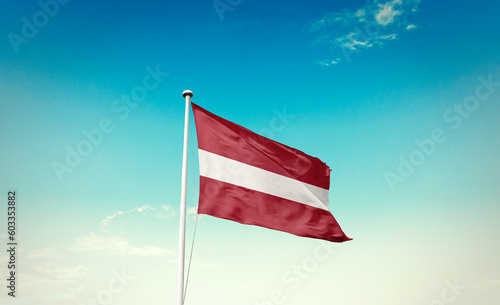 Waving Flag of Latvia in Blue Sky. The symbol of the state on wavy cotton fabric.