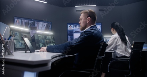 Wallpaper Mural Male security officer touches tablet and controls CCTV cameras with AI face scanning. Computer monitors and big digital screens showing security cameras footage. Female colleague works at background. Torontodigital.ca
