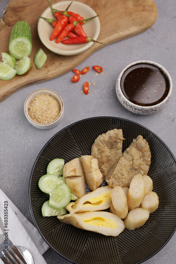 Pempek Palembang, an Indonesian traditional cuisine made from fish cake served with sweet spicy sour sauce and diced cucumber. Piled on white plate on the table Pempek Palembang, an Indonesian traditional cuisine made from fish cake served with sweet spicy sour sauce and diced cucumber. Piled on white plate on the table