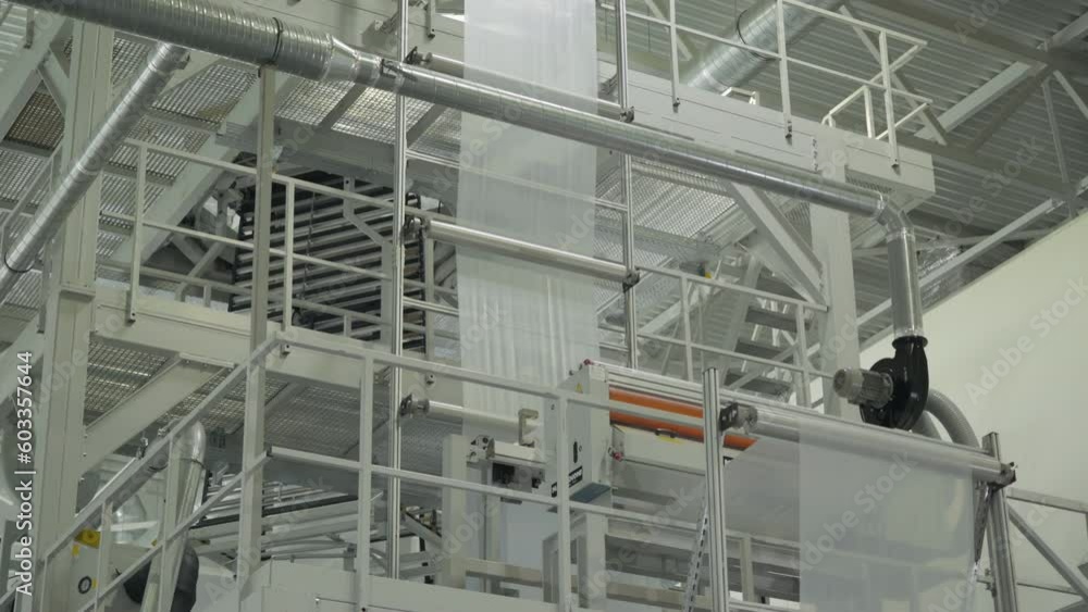 Factory machinery processing the white raw plastic material. Factory machinery stretching the material for processing. Factory machinery rollers processing the transparent plastic film. Factory machinery processing the white raw plastic material. Factory machinery stretching the material for processing. Factory machinery rollers processing the transparent plastic film.