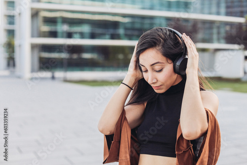 Young woman with black headphones listens to the music her closed eyes, enjoying and dancing on the street 