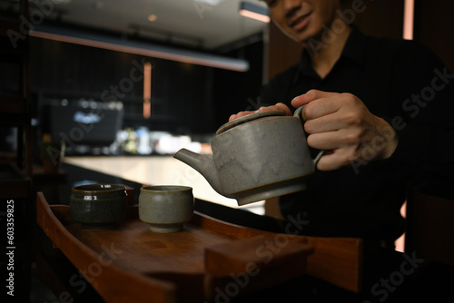 Close up and cropped image of Young Asian pour tea from the clay pot into the teacup.