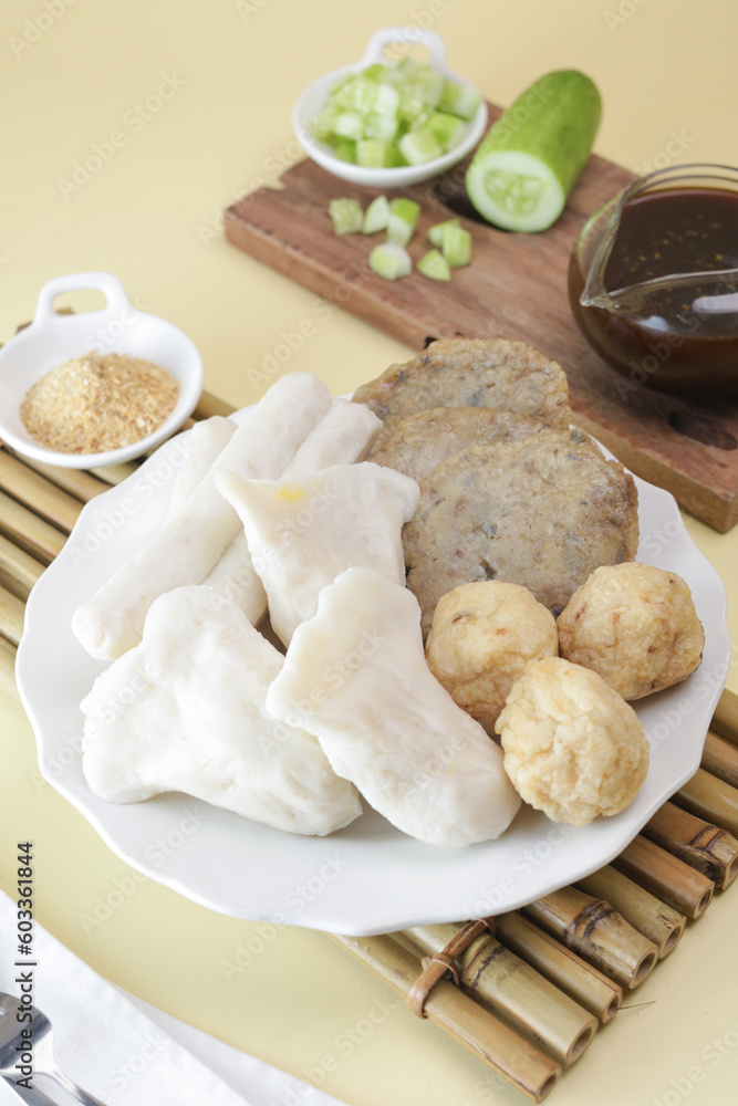 Pempek Palembang, an Indonesian traditional cuisine made from fish cake served with sweet spicy sour sauce and diced cucumber. Piled on white plate on the table Pempek Palembang, an Indonesian traditional cuisine made from fish cake served with sweet spicy sour sauce and diced cucumber. Piled on white plate on the table