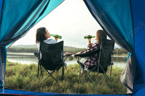 Fotografie, Obraz Asian LGBTQ+ couples drinking drinks in a romantic atmosphere inside a camping tent, LGBTQ couples watching nature, rivers, forests, camping atmosphere
