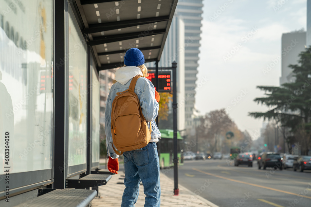 Millennial gut tourist with backpack waiting at bus stop, male passenger using public transportation in city. Teenage boy commuting to college by public transport in morning