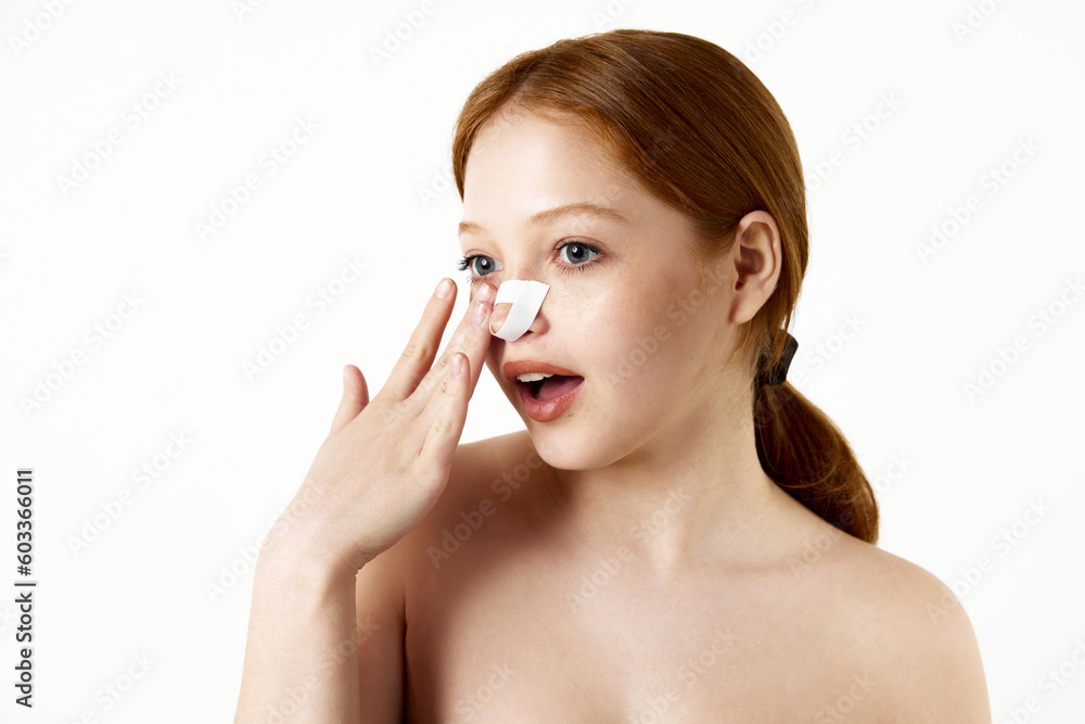 Impressed, happy, young girl with a bandage on her nose after rhinoplasty with a mirror against white studio background. Concept of beauty, plastic surgery, rhinoplasty care, cosmetology, health Impressed, happy, young girl with a bandage on her nose after rhinoplasty with a mirror against white studio background. Concept of beauty, plastic surgery, rhinoplasty care, cosmetology, health