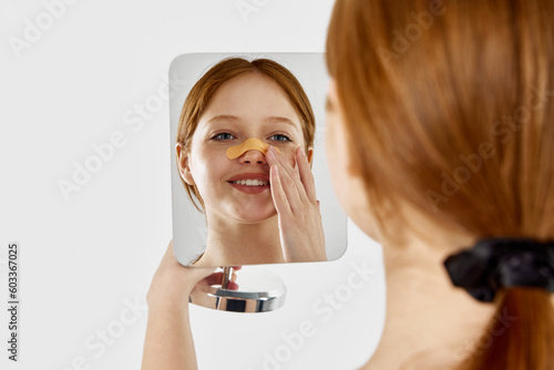 Εκτύπωση καμβά Happy, young, beautiful girl with bandage on her nose after rhinoplasty looking at mirror against white studio background