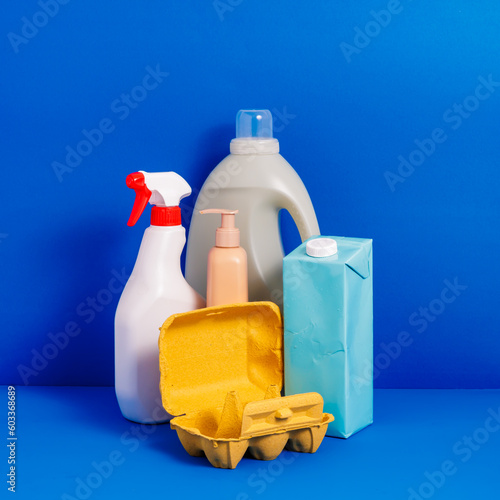 Generative AI illustration of plastic bottles placed near carton egg container on blue background representing concept of recycling packaging photo