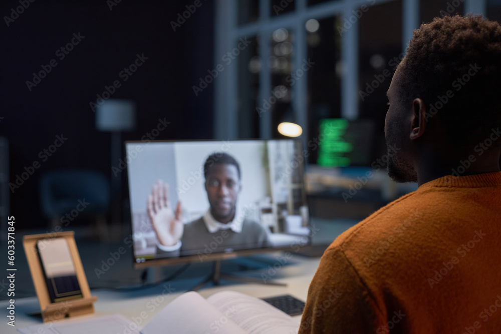 African American businessman having video call on computer with his colleague while working in office till late night - obrazy, fototapety, plakaty 