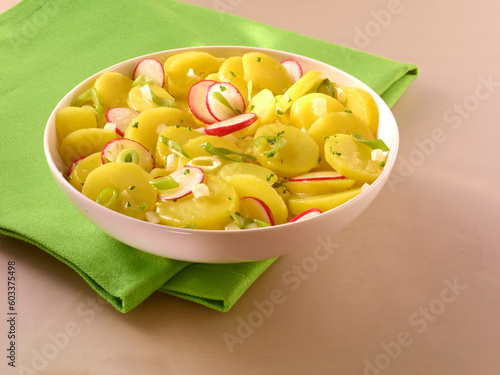 Kartoffelsalat mit Radieschen Essig und Oel in weisser Porzellanschale mit gruener Serviette photo
