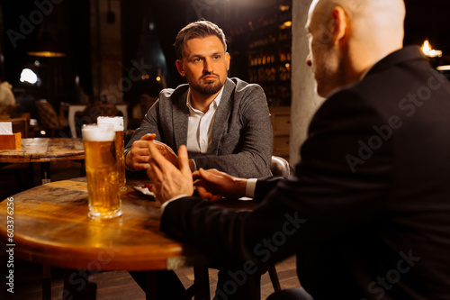 two adult friends talking while sitting in a pub. Two men drink draft beer, celebrate meeting and talk after work