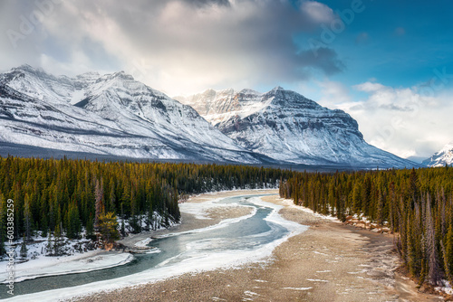 Rocky Mountains with frozen river flowing through pine forest in winter