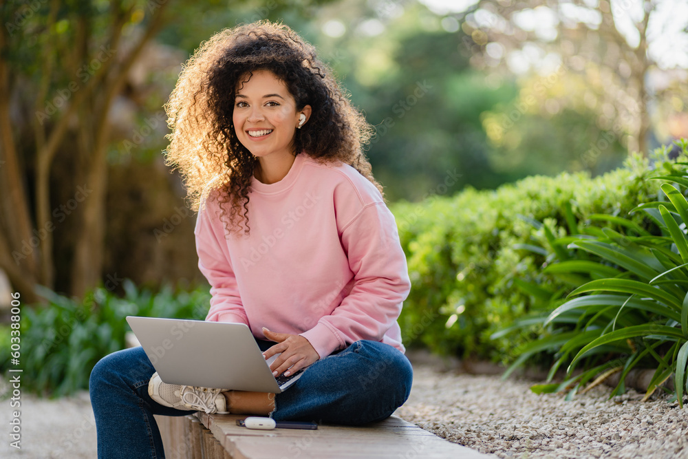 Obraz premium pretty curly young woman sitting in park working on laptop remote job