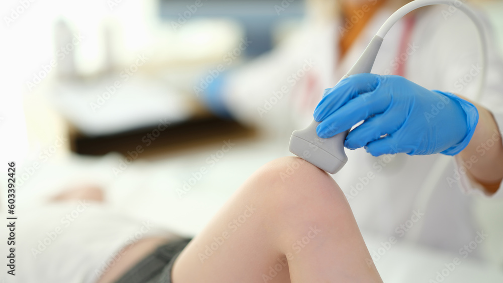 Doctor putting ultrasound probe on child knee in clinic closeup. Instrumental diagnosis of diseases of bones and muscles in children concept - obrazy, fototapety, plakaty 