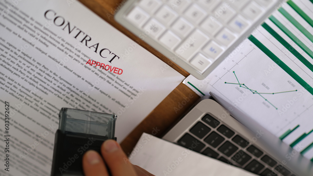 Manager hand putting red stamp approved on contract document closeup. Approval of business deals and employment concept Manager hand putting red stamp approved on contract document closeup. Approval of business deals and employment concept
