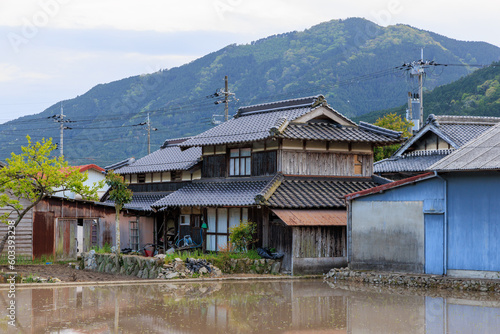 Traditional Japanese wooden house by flooded rice field in small town