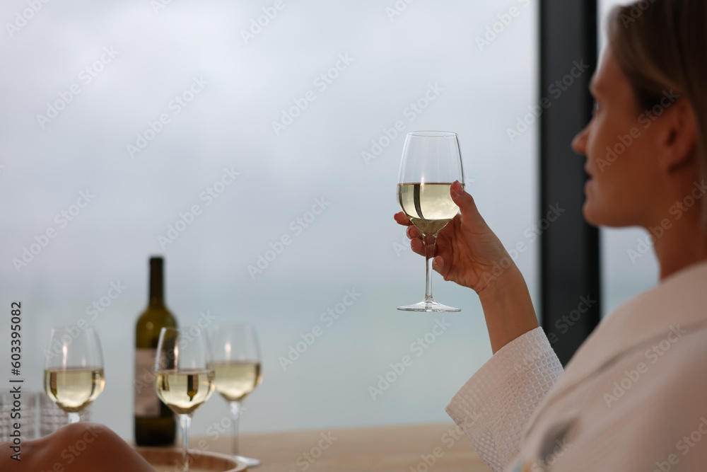 Woman in bathrobe holding glass of white wine closeup. Rest and relaxation in hotel concept Woman in bathrobe holding glass of white wine closeup. Rest and relaxation in hotel concept