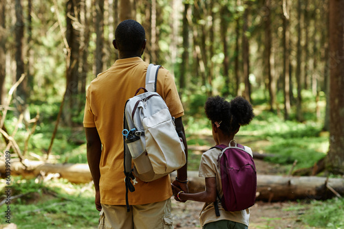 Rear view of family of two with backpacks hiking in the forest together in summer day