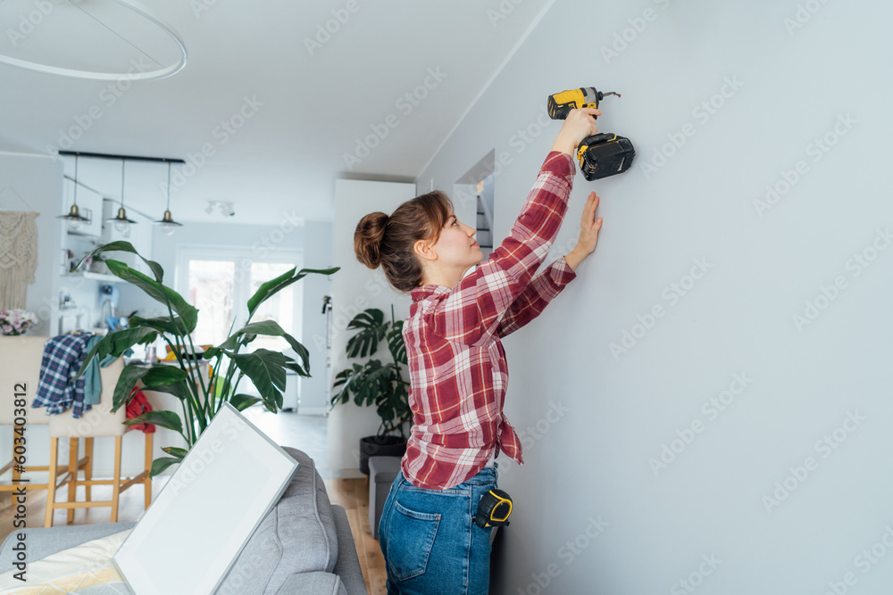 Back view young woman screwing screw into wall with electrical