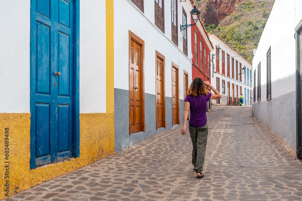 Woman walking past colored doors and windows to the streets in the village of Agulo in the north of La Gomera in summer, Canary Islands