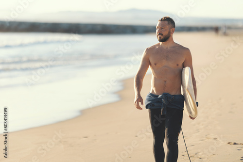 An athletic man surfer with naked torso walking on the seashore