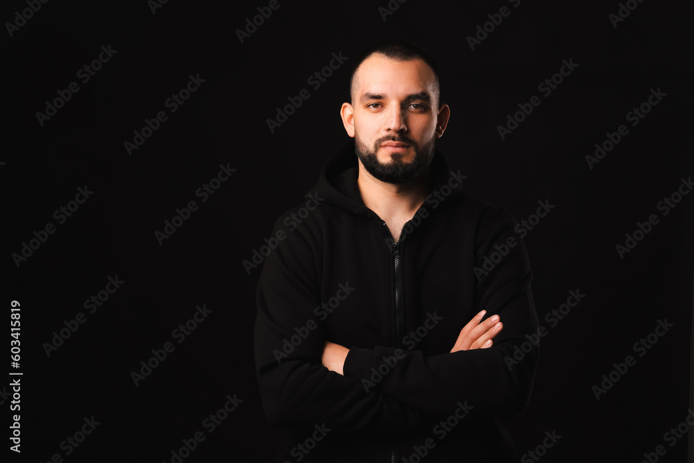 Dramatic portrait of a strong young man in black standing with arms crossed. Studio shot.