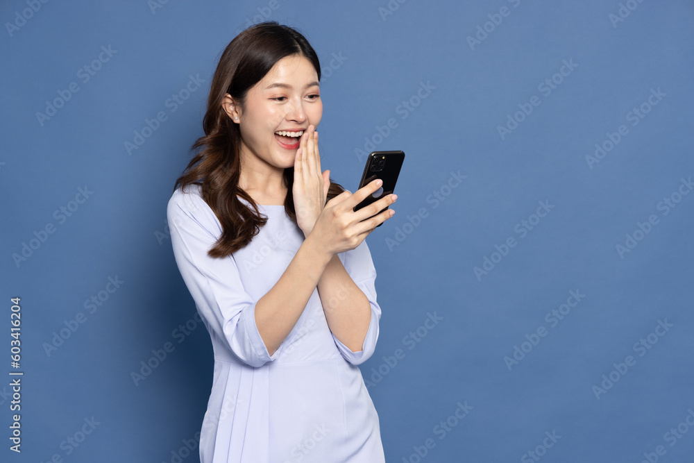 Happy Asian businesswoman typing or using mobile phone isolated on blue background Happy Asian businesswoman typing or using mobile phone isolated on blue background
