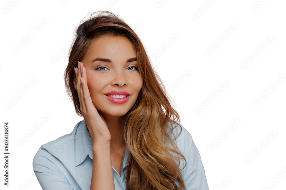 Photo of pleasant looking female model touches cheeks with palm, has gentle toothy smile, wears makeup, dressed in casual shirt, stands against purple wall, copy space area for your advertisement