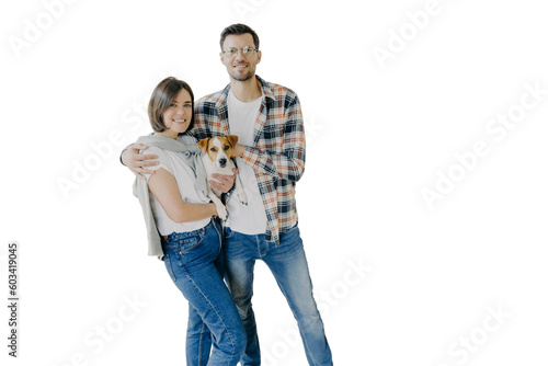 Happy woman and man tenants or renters of flat pose in own house, cuddle and pose with little dog, have glad expressions, start living in new bought apartment. Family and relocation concept.
