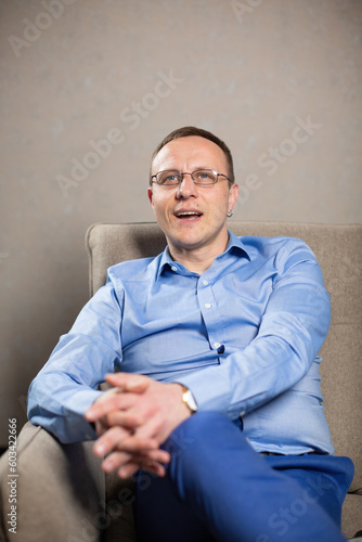 Male psychologist talks on therapy session sitting in comfortable chair. Man in glasses gives professional advices to client in office